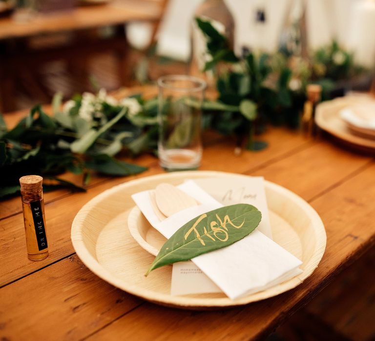 Wooden wedding plates with green leaf table names, foliage decor and cork stopped tequila wedding favours