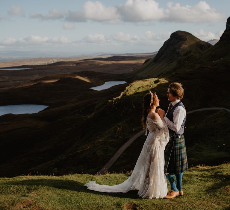 Bride & groom stand on lush greenery whilst looking over hills