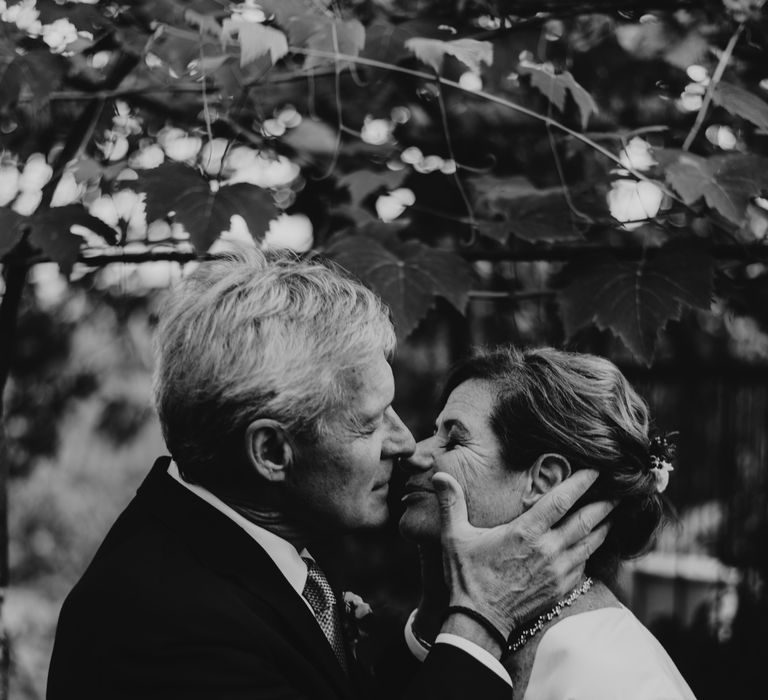 Groom holds brides face in his hands as he leans in to kiss her on their wedding day in black & white image