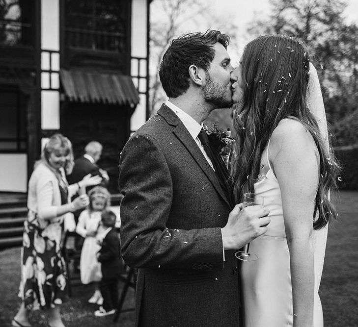 Black and white portrait of the bride and groom kissing after the confetti moment 