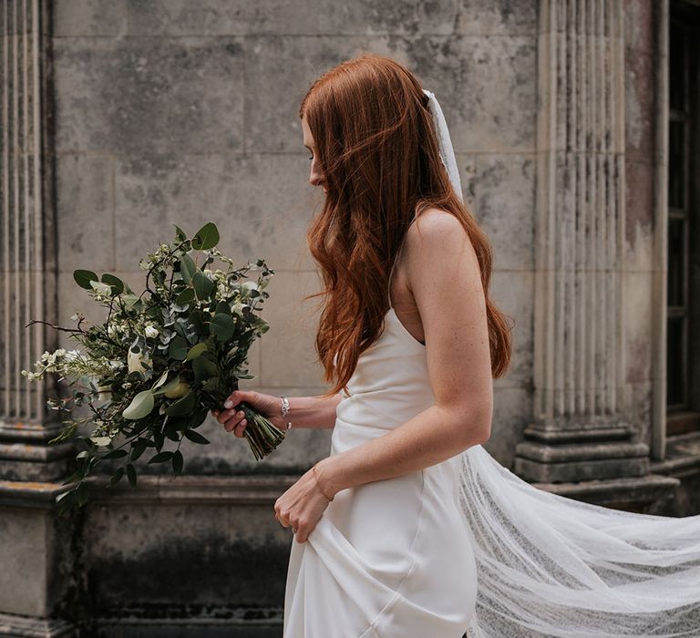 Beautiful bride in a satin slip Grace Loves Lace wedding dress with long wavy red hair and a delicate lace cathedral length veil 