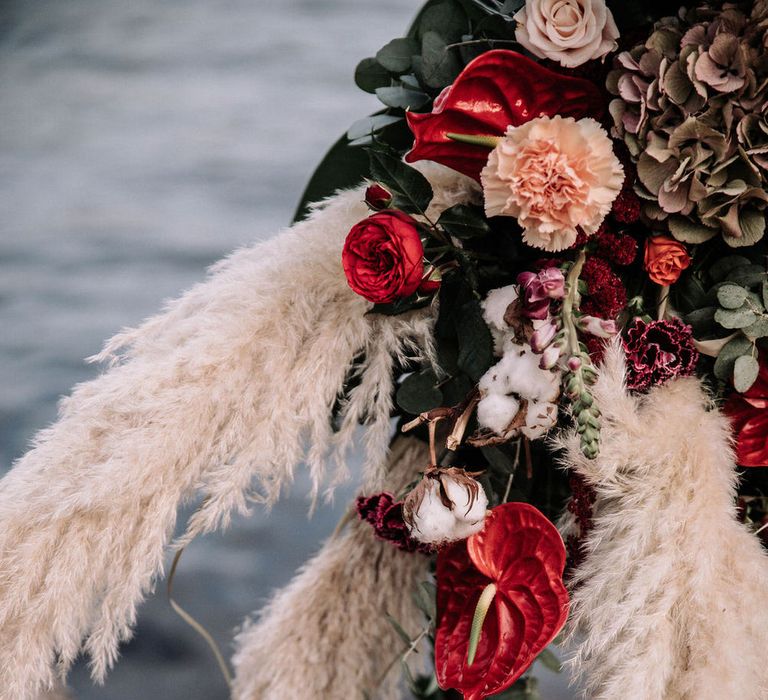 Red anthuriums, roses, pampas grass, dried hydrangea, pink carnations, eucalyptus and palm leaves