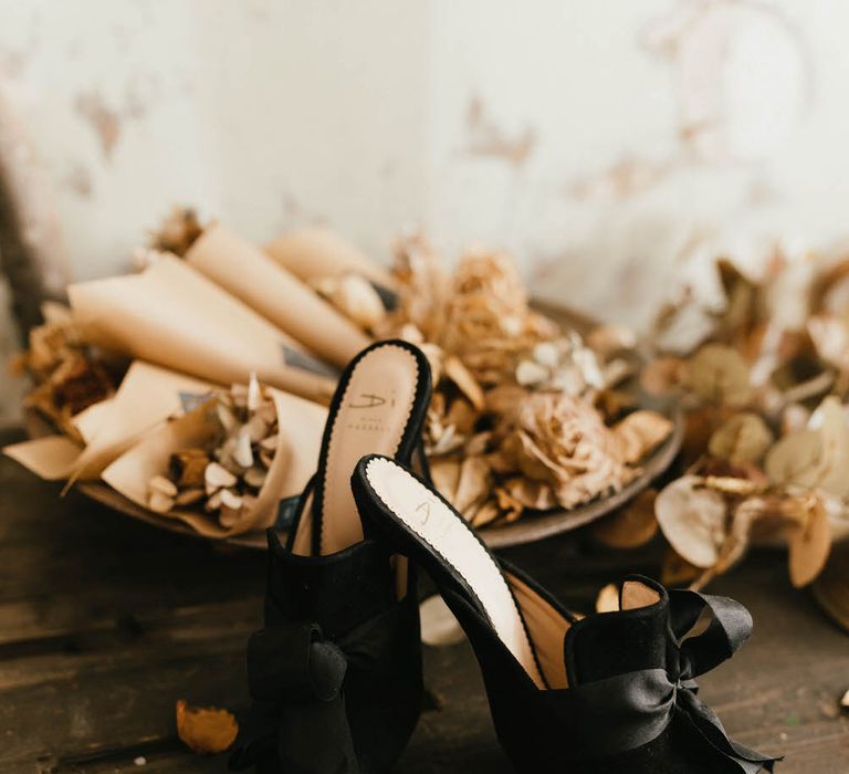 Black velvet pointed toe heeled mules with ribbon detail, next to dried flower confetti