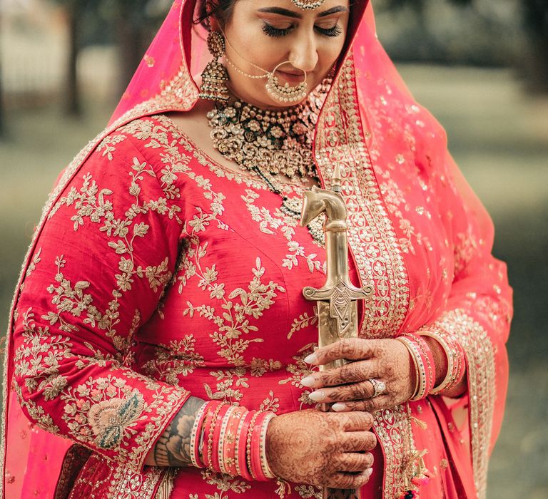 Bride looks down as she wears traditional Lengha in brightly coloured red fabric and gold embellishments 