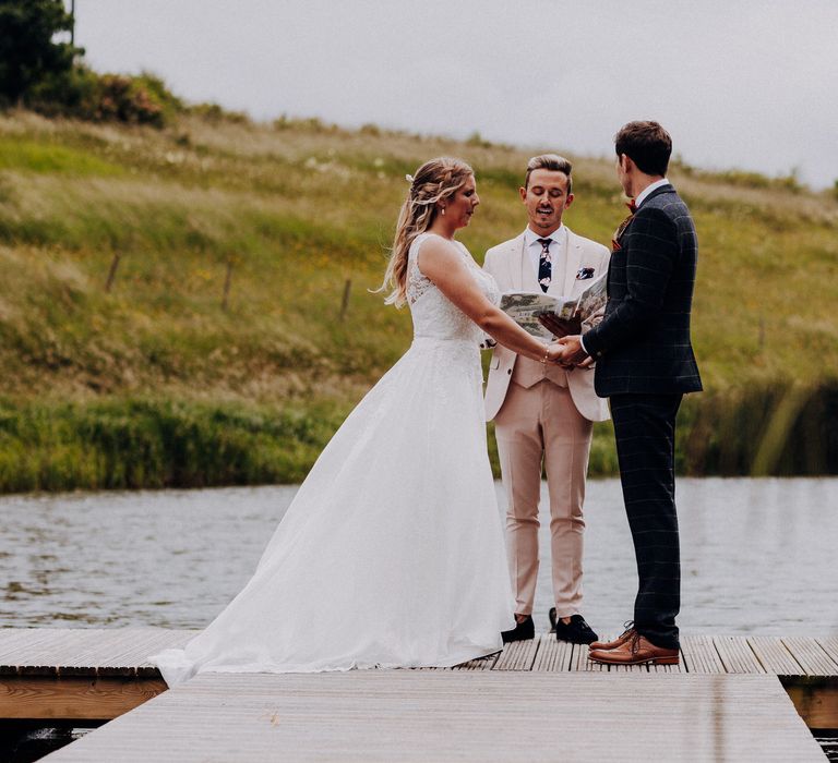 Bride & groom hold hands and look toward friend who is marrying them on their wedding day