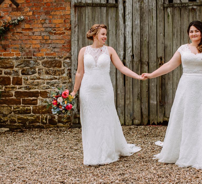 Brides look lovingly at one another as they hold hands and smile on their wedding day 