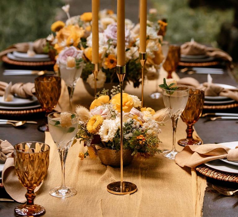 Wedding table decor with yellow table runner, gold candles sticks and yellow taper candles and floral arrangements 