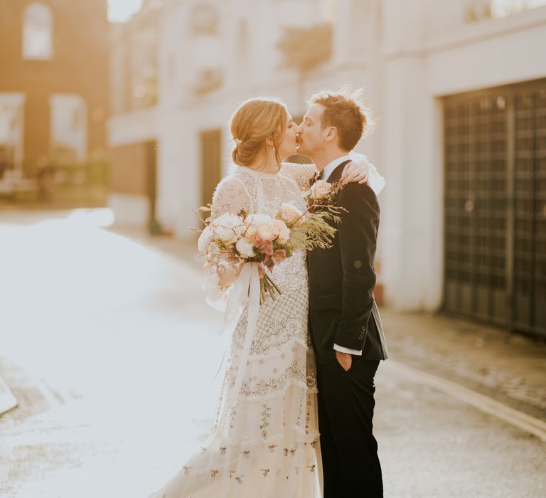 Bride & groom kiss as the sun shines around them and bride wears Needle And Thread wedding dress