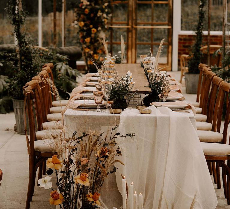 Tabelscape in a conservatory with natural linens, orange and yellow flowers and brass accents 