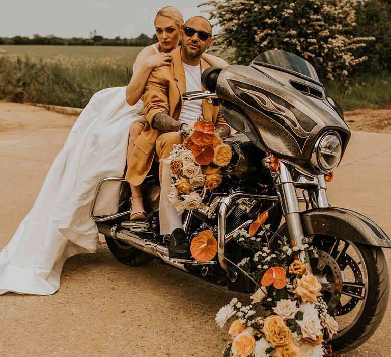 Stylish bride in a Princess wedding dress and groom in a mustard suit sitting on a Harley Davidson motorcycle 