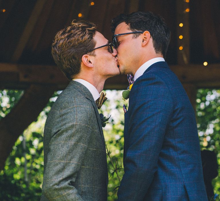 Grooms kiss outdoors during wedding ceremony | Story + Colour