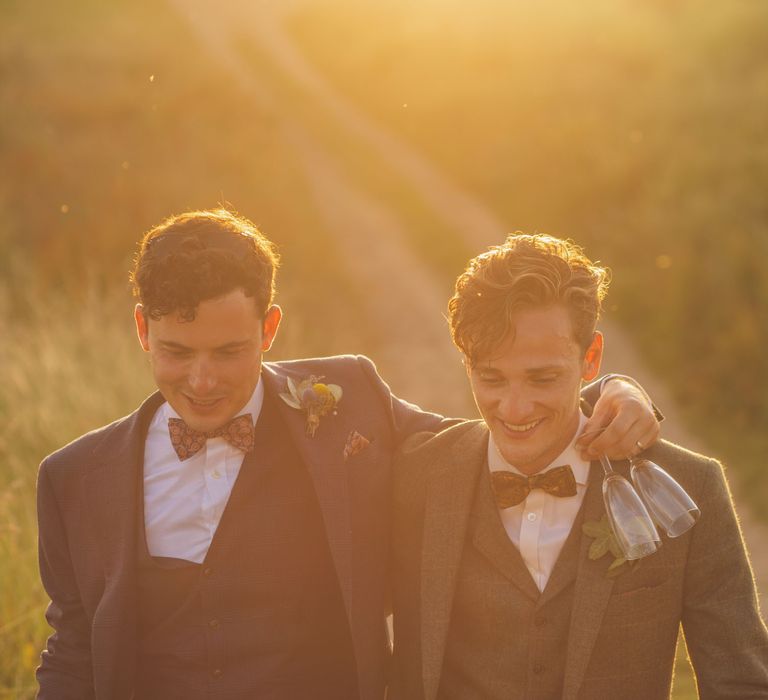 Grooms walk through lawns as the sun sets behind them on their wedding day | Story + Colour