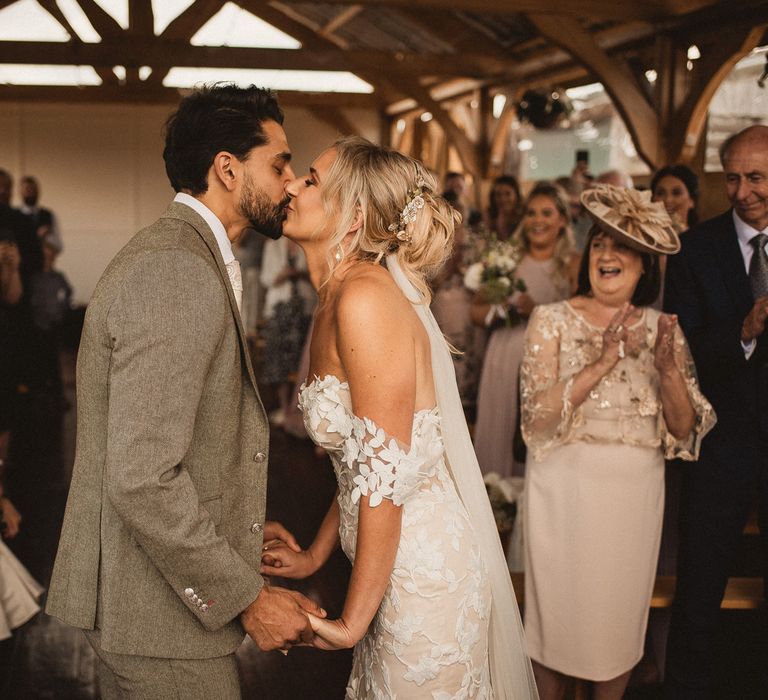 Bride in off the shoulder Enzoani wedding dress kisses groom in grey suit during Inkersall Grange Farm wedding ceremony