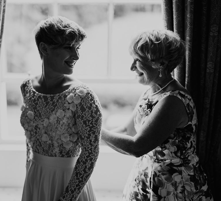 Mother of the bride doing her daughters appliqué wedding dress up with long sleeves on the wedding morning 