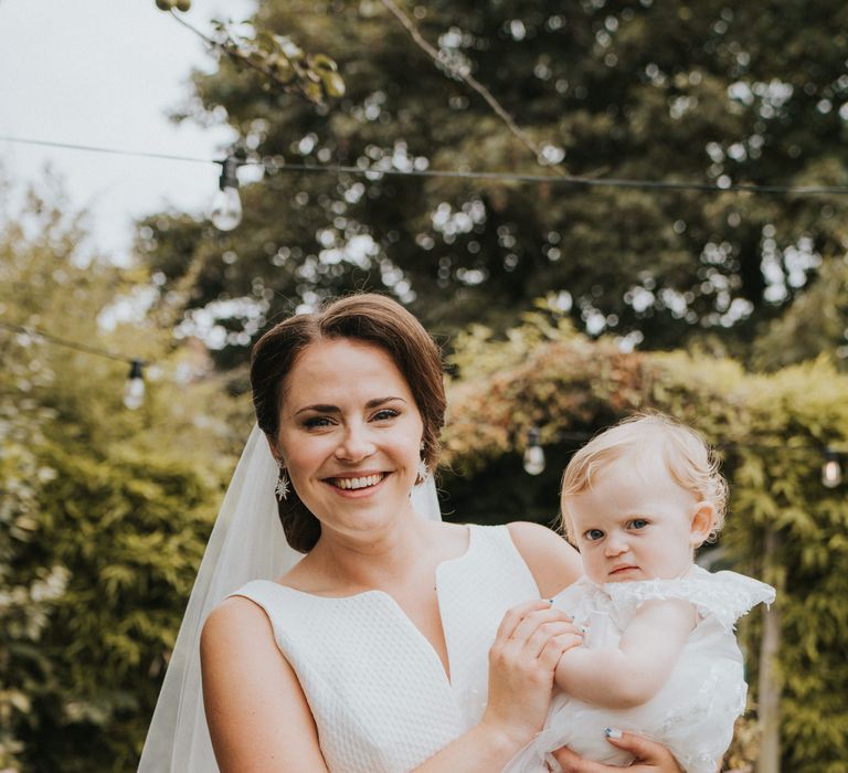 Bride carries flower girl in white dress