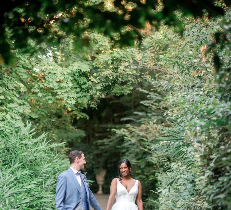 Indian bride walks with her husband through floral archway whilst wearing white wedding gown in Lake Garda