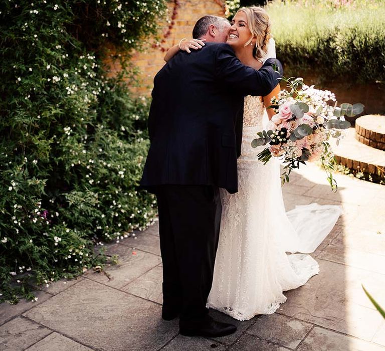 Bride clutches pink bouquet as she hugs family at wedding