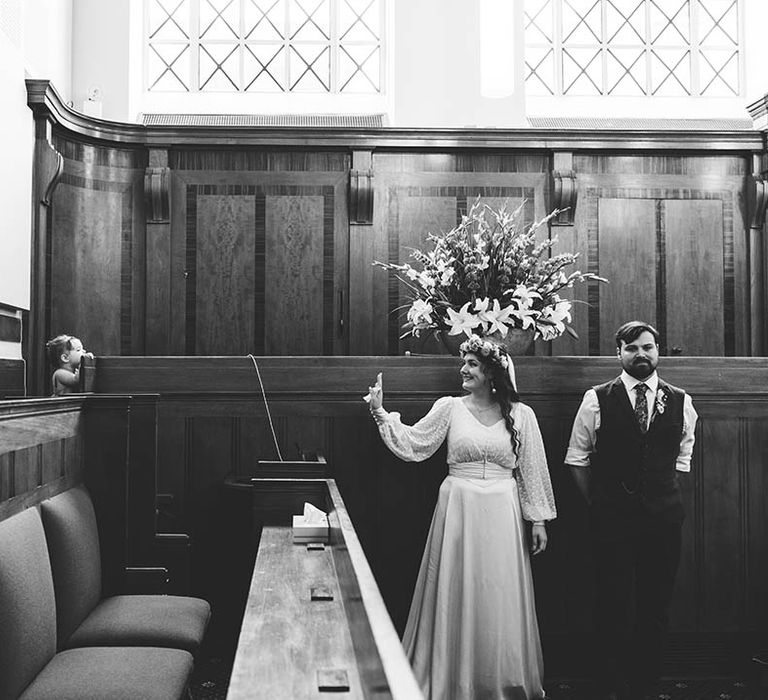 Black & white image of bride waving at flower girl during wedding ceremony