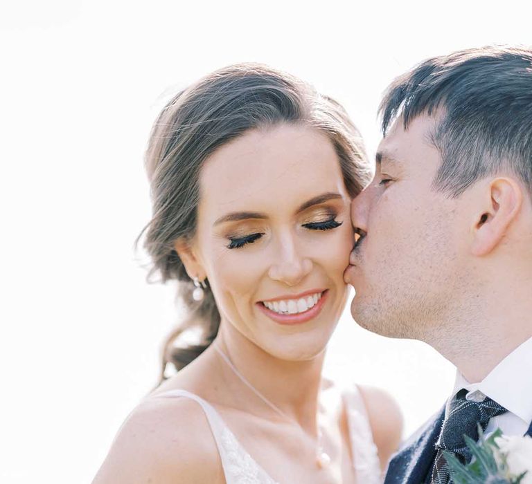 Groom kissing his bride with shimmering gold eyeshadow and false eyelashes wedding makeup 