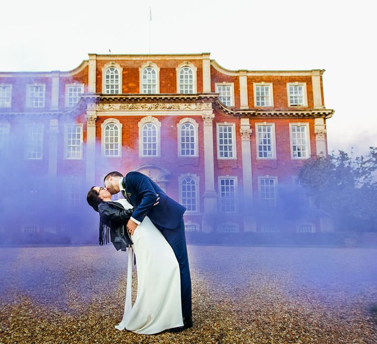 Bride & groom kiss outdoors as purple smoke bomb surrounds them