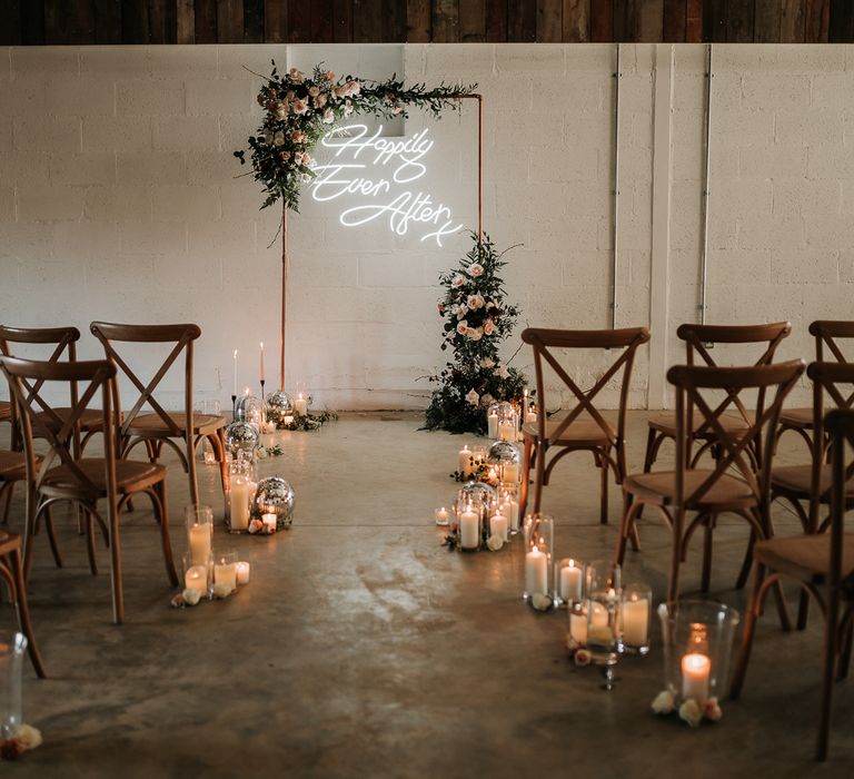 Candle lit aisle complete with wooden chairs and neon sign 'Happily Ever After'