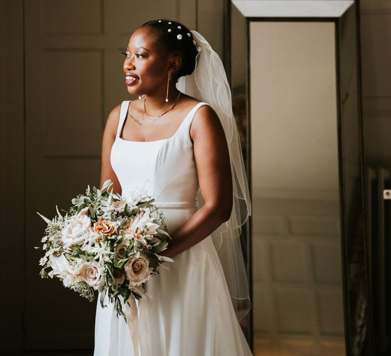 Black bride with short hair decorated with peal clips in an Essense of Australia wedding Dres with straps looking out the window 