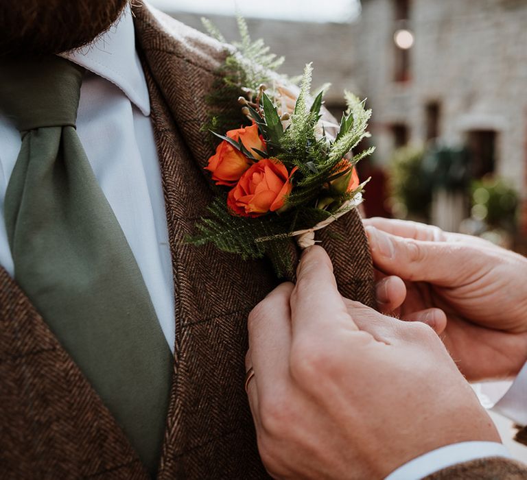 Groom has his floral buttonhole in orange applied to blazer on wedding day