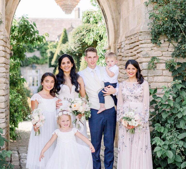 Bride & groom stand with wedding party under archway and chandelier outdoors on their wedding day 