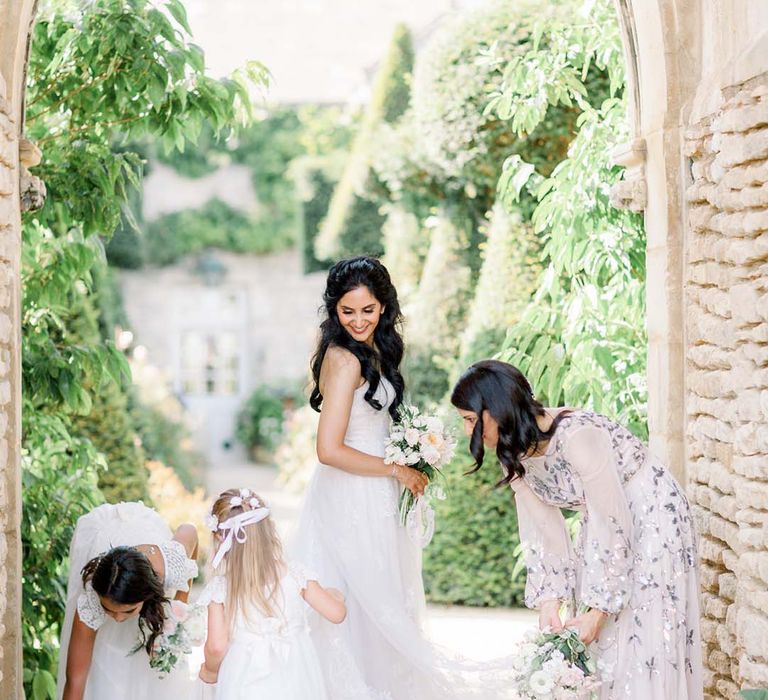 Bride stands with her wedding party outdoors as they move her wedding gown train outdoors 