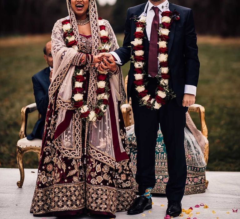 Bride wears Indian burgundy saree wedding dress and groom matches in his burgundy tie adding a pop of colour at his socks