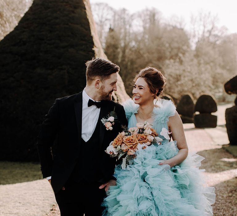 Black tie wedding with groom in a tuxedo and bride in a coloured wedding dress holding a peach and cafe au late bridal bouquet 