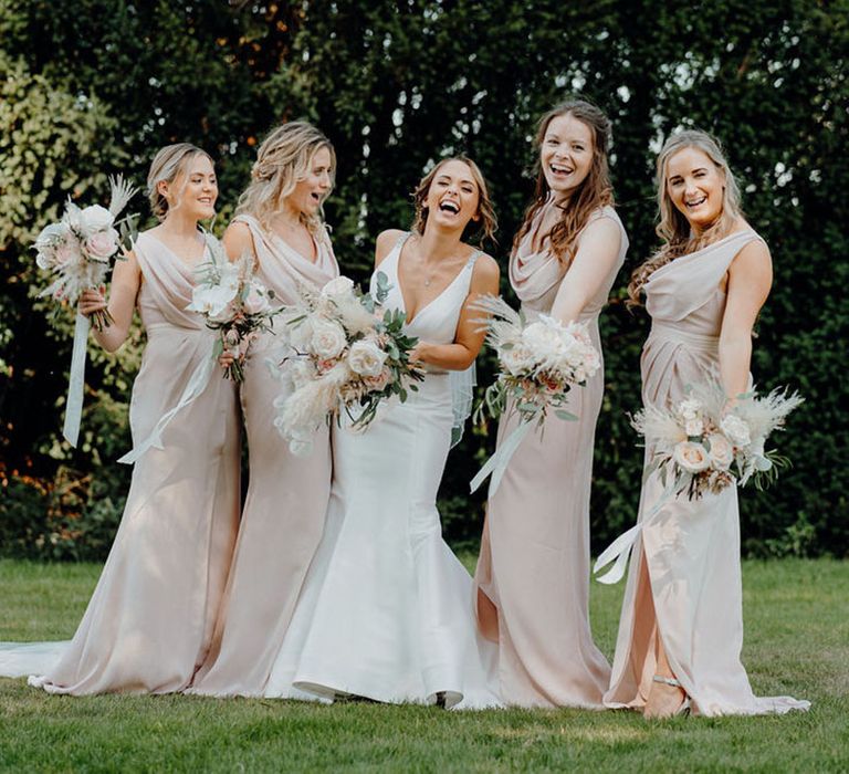 Bride and bridesmaids holding pink flower bouquets in long pink bridesmaid dresses from ASOS