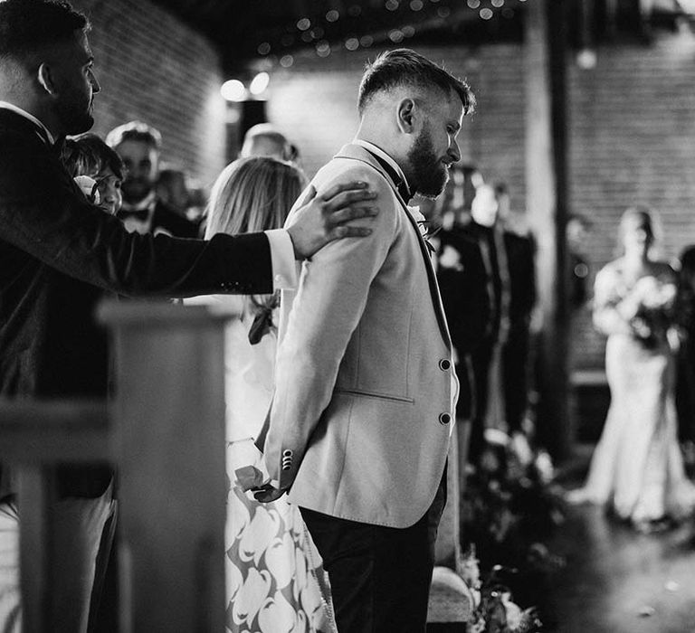 Groom gets ready to see his bride for the first time as she walks into rustic barn wedding