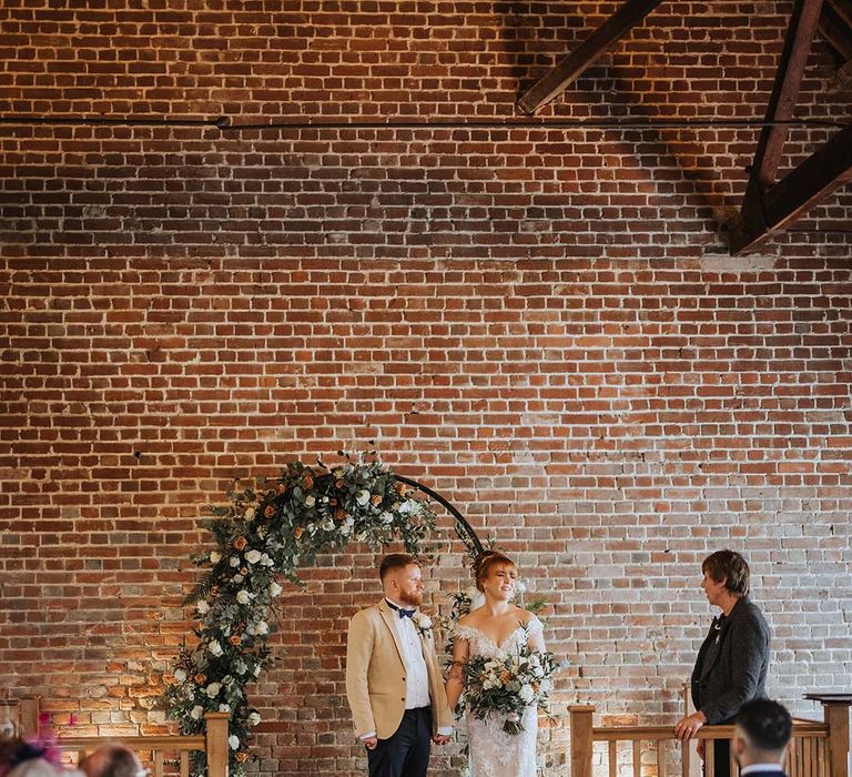 Bride and groom at the altar with white and orange coloured wedding flowers at rustic barn 