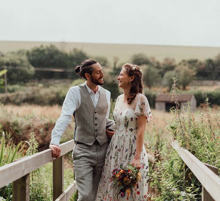 Bride and groom smiling together with bride holding colourful pink, purple, red, yellow, orange wedding bouquet 