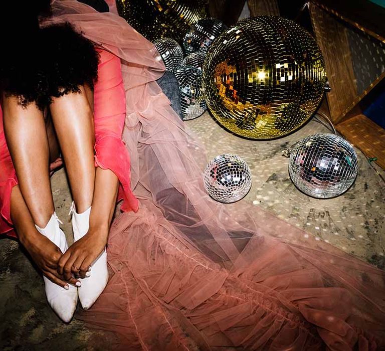 Bride in a red wedding dress with pink veil and white boots sitting next to silver and gold disco balls at The Canary Shed wedding venue 