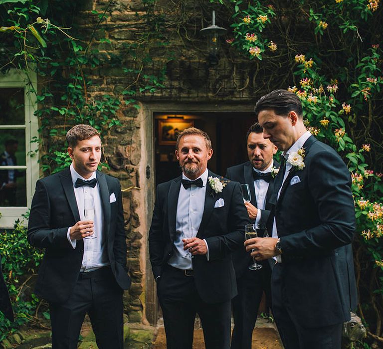 Groom stands with groomsmen in matching black tie outfits for classic style wedding