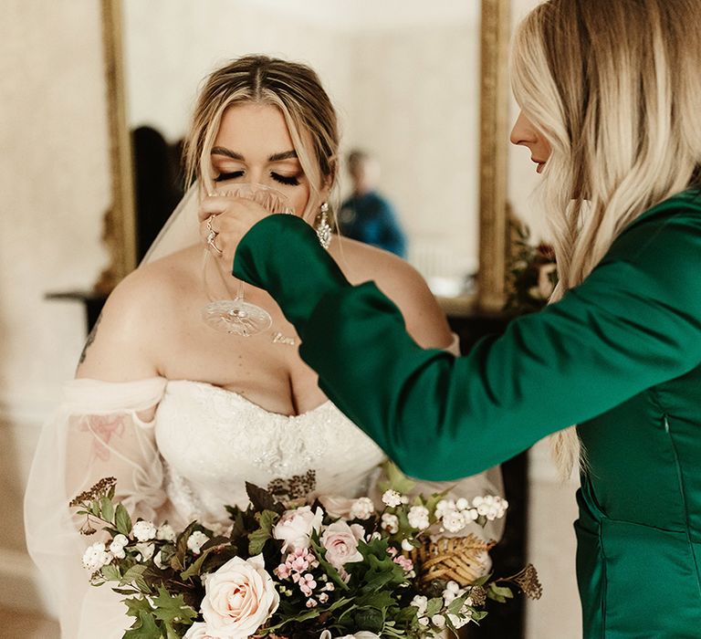 Bride has a quick drink of courage before the ceremony as bridesmaid in emerald green dress lifts the glass