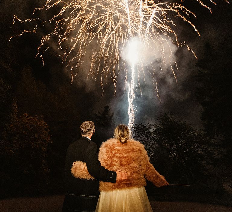 Bride and groom stand with their arms around each other as they watch the firework entertainment