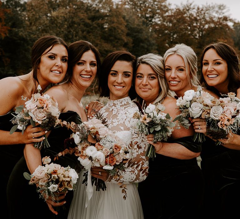 Bride smiles with all of her bridesmaids holding their autumnal bouquets