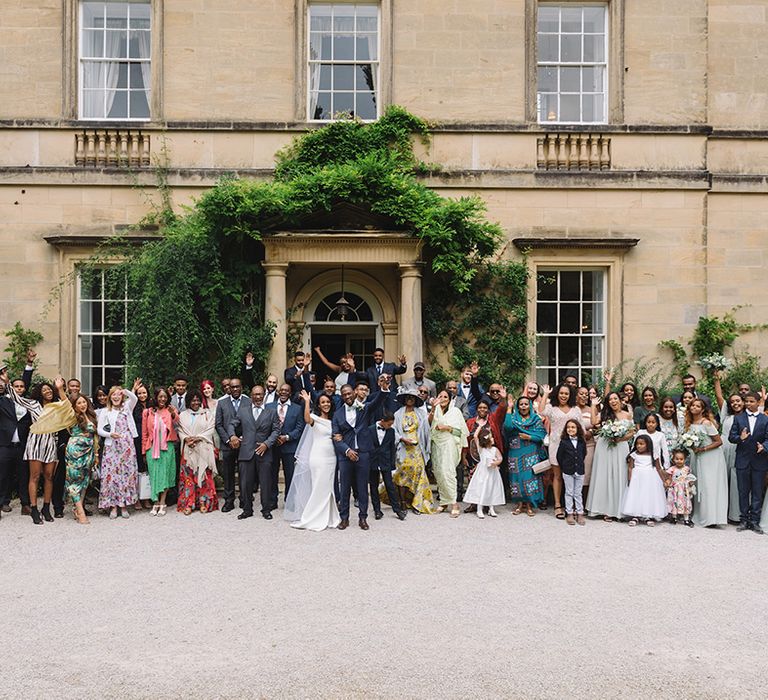 Bride and groom wave with all of their wedding party standing outside the venue