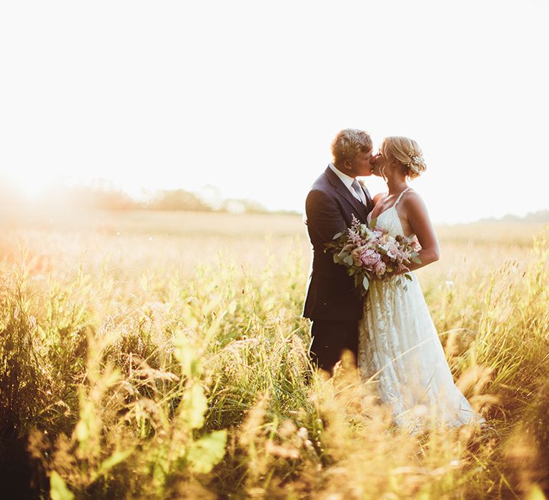 Bride in boho lace wedding dress and groom in blue suit kiss each other in fields at South Downs National Park 