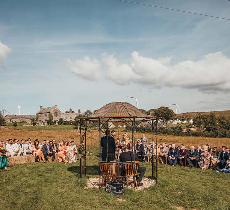 Outdoor wedding ceremony at The Ash Barton Estate with wedding guests seated on hay bales