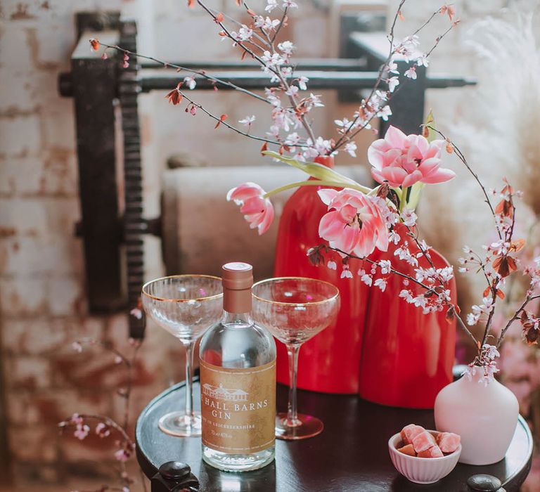 Side table with two coupe champagne glasses, cherry blossom and flower stems in vases 