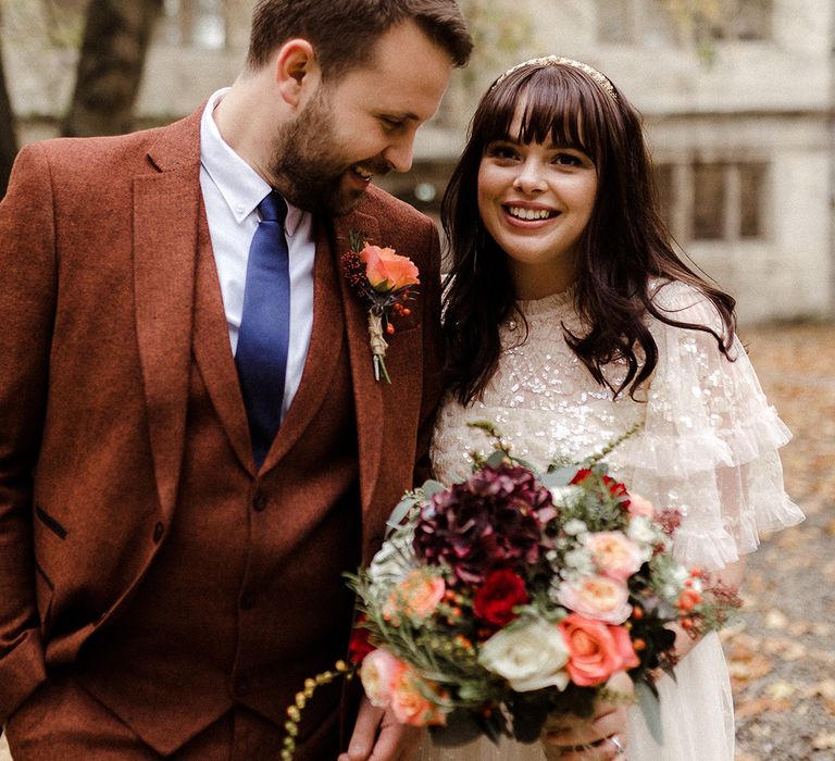 Smiling bride holding rose and hydrangea wedding bouquet with groom with matching rose buttonhole with berries 