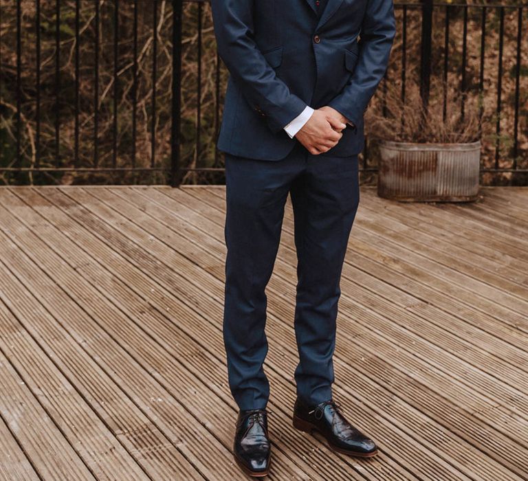 Groom smiles wearing dark blue suit and patterned floral tie for industrial wedding in spring