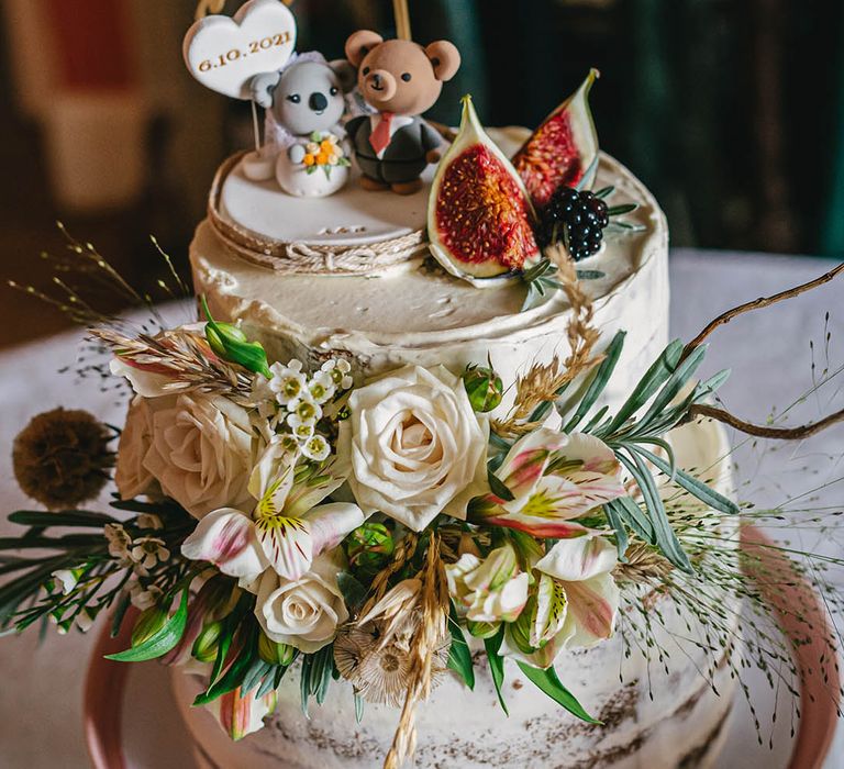 Two tier semi-naked wedding cake decorated with flowers with personalised cake topper and koala and bear figures 