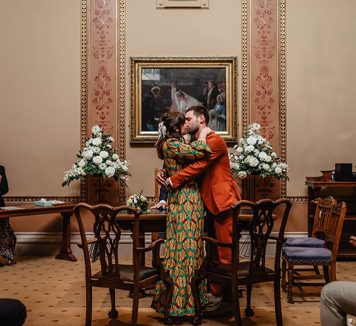 Bride wearing brightly coloured La Double J wedding gown & groom in orange Paul Smith suit kiss at Bristol Register Office 