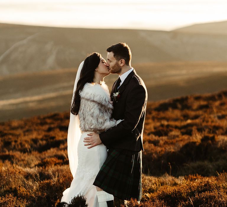 Bride & groom embrace on Scottish hills during sunset on their wedding day