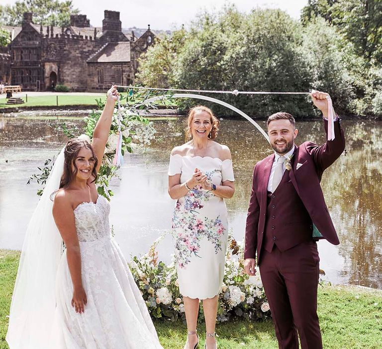 Outdoor handfasting ceremony at East Riddlesden Hall with bride in a princess wedding dress and groom in a burgundy suit